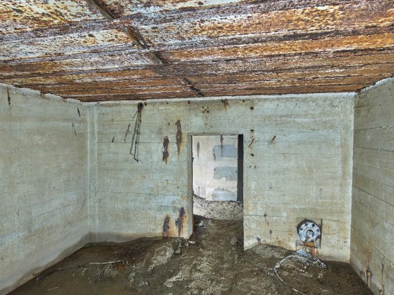 Vue du magasin à munitions situé au sud. Sur le mur du fond : câblage électrique pour l'alimentation des plafonniers et à droite, bouche de surpression à clapet à contrepoids