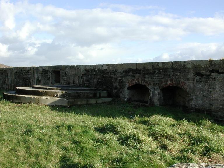 Vue de la batterie basse du Mengant : plate-forme en béton pour canon et niche en béton (état en 2009). A droite, deux niches en pierre de taille et brique aménagées dans l'épaisseur du parapet