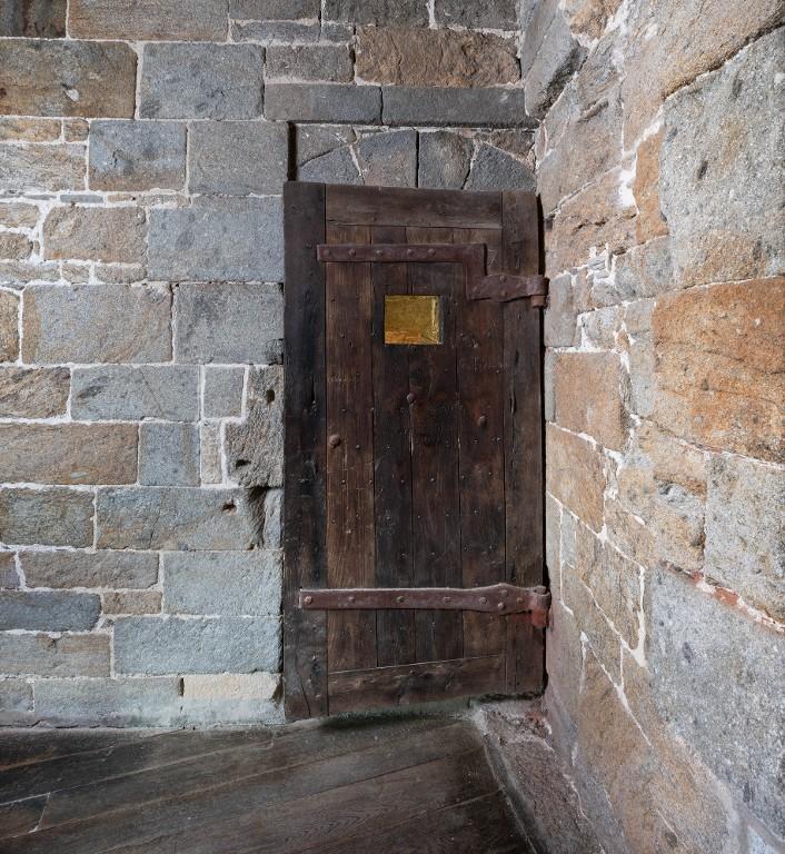 Vue intérieure de la tour Solidor : premier étage, pièce intermédiaire, porte d'accès depuis l'escalier en vis (fermée). Le dispositif de fermeture de la porte et le judas témoignent de l'utilisation carcérale de la tour. Elle comporte plusieurs graffitis