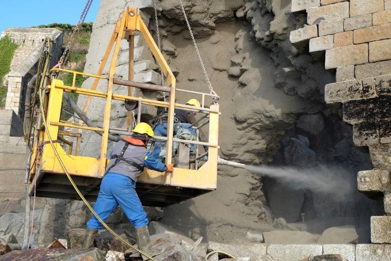 Vue des travaux de consolidation de 2015 : du béton est projeté sur la maçonnerie de la brèche de la batterie basse par des techniciens travaillant avec une nacelle suspendue